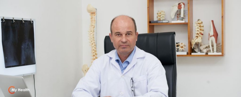 4 סיבות למה מקבלים קילה? - ניתן לראות רופא עם קרחת וחלוק לבן אשר יושב בשולחן העבודה שלו ומביט למצלמה. בצד שמאל למטה לוגו אתר my-health